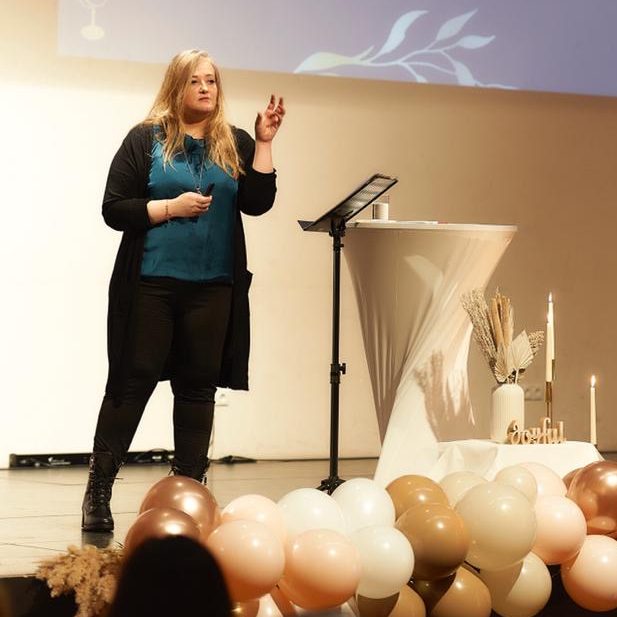 Frau spricht am Podium mit Dekoration aus Luftballons im Vordergrund.