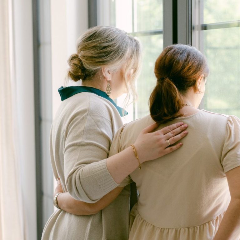 Zwei Frauen stehen zusammen am Fenster und halten sich tröstend im Arm
