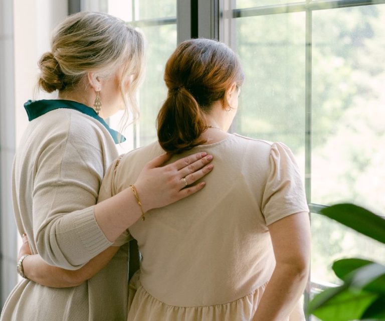 Zwei Frauen stehen gemeinsam am Fenster und blicken nach draußen.