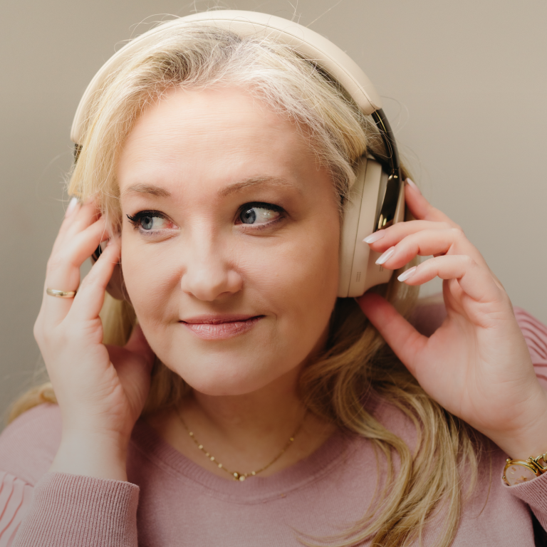 Frau mit Mikrofon lächelt, trägt eine grüne Bluse und sitzt in einem gemütlichen Raum.