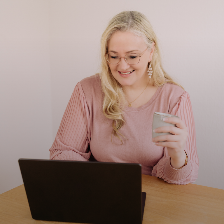 Lächelnde Frau sitzt an einem Tisch, hält ein Mikrofon und arbeitet am Laptop.