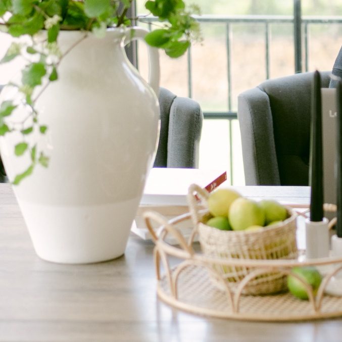 Vase mit Pflanzen und Obstschale auf einem Holztisch in einem modernen Raum.